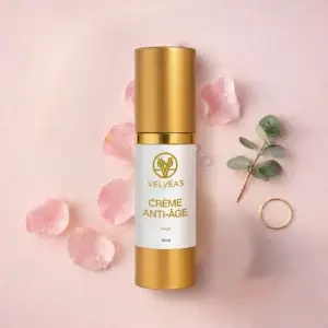 Flacon Velvéas Crème Anti-Âge Face 50 ml entouré de pétales de rose, branche d'eucalyptus et alliance dorée sur fond rose pâle